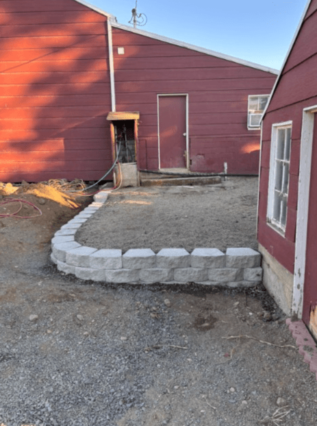 Newly built curved retaining wall with gray block pavers beside a red-sided home