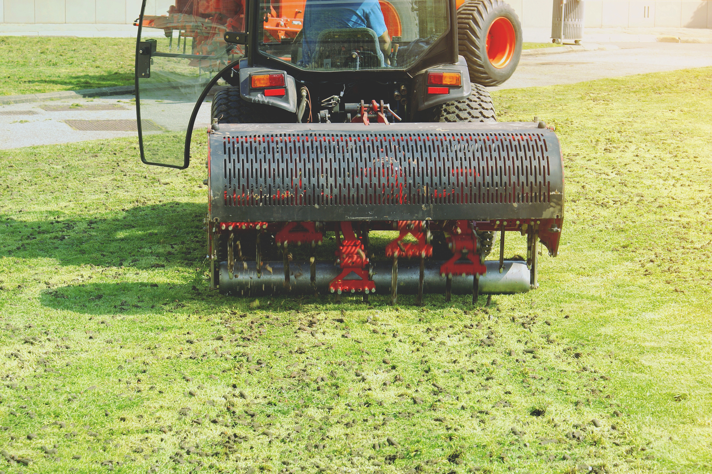 Tractor pulling a core aerator across a green lawn, leaving soil plugs behind