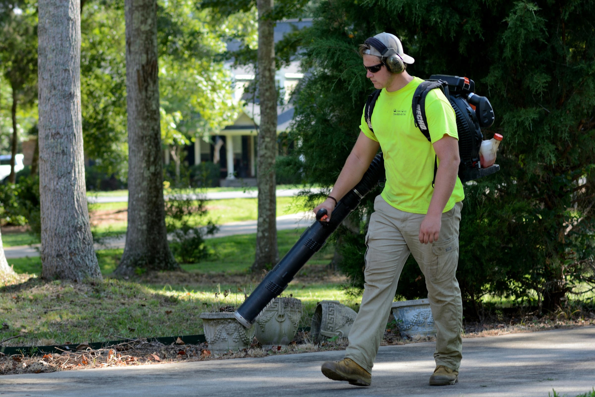Worker using a backpack leaf blower on a residential driveway