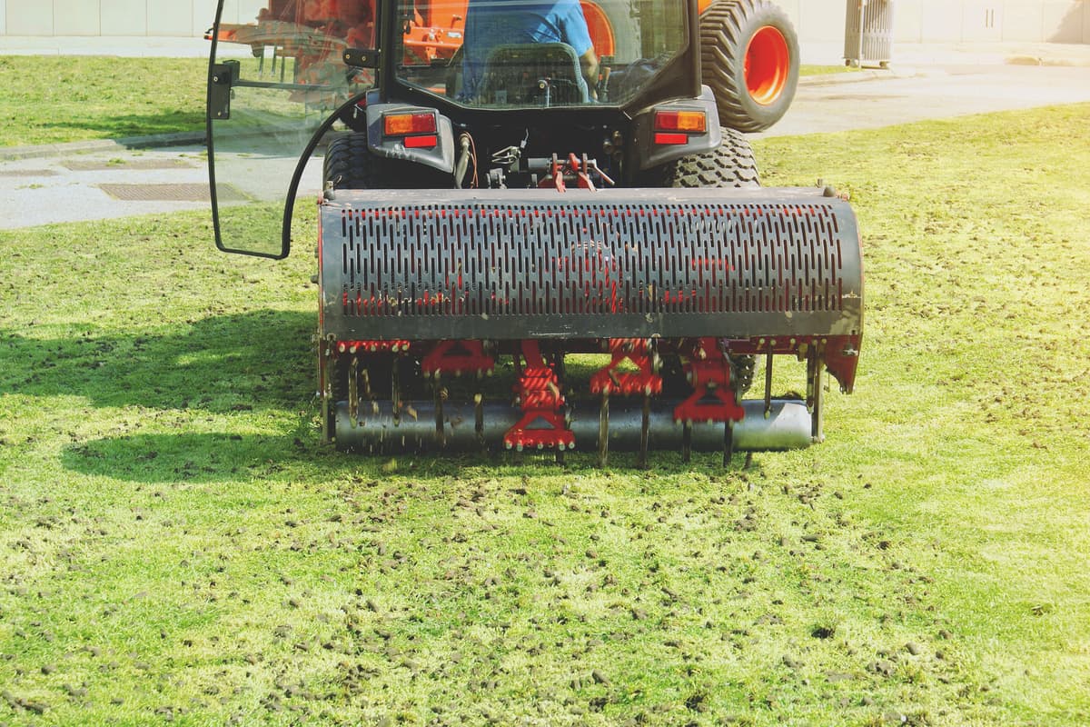 Tractor pulling a core aerator across a green lawn, leaving soil plugs behind