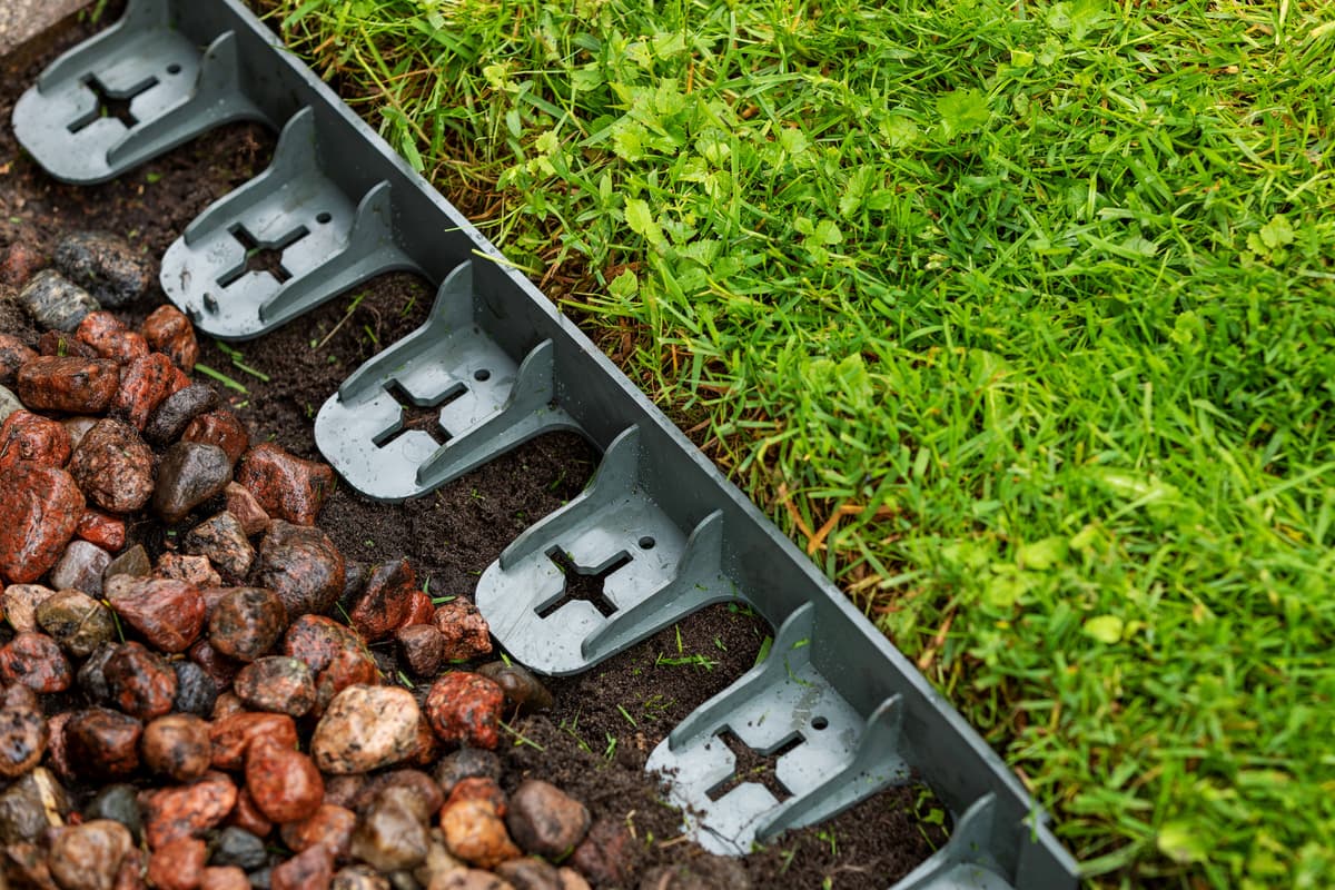 Plastic lawn edging being installed between grass and a decorative rock border